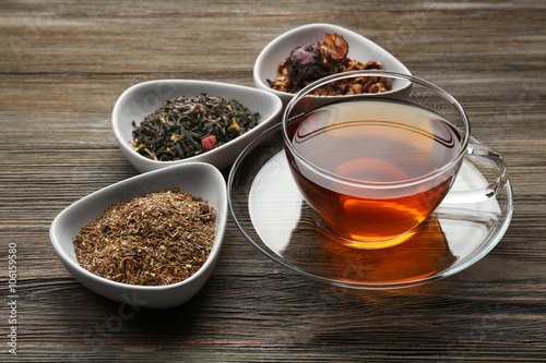Tea concept. Different kinds of dry tea in ceramic bowls. Glass cup of tea on wooden background