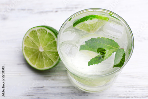 Fresh cocktail with ice, mint and lime on white wooden table background