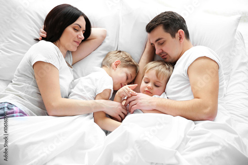 Family sleeping in bed unde...