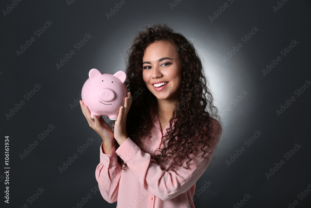 Beautiful young girl holding piggy bank on grey background Beautiful young girl holding piggy bank on grey background