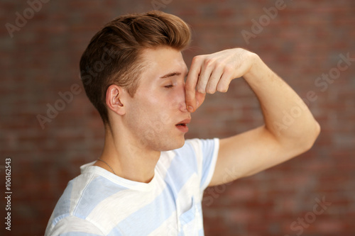 Φωτογραφία Young blonde man pinching his nose because of the stench on brick wall backgroun