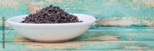 Loose dried darjeeling black tea leaves in white bowl over wooden background