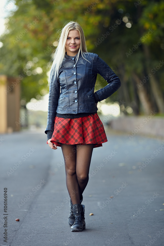 Young trendy dressed blonde woman showing her weekend outfit having fun and posing on park path shallow depth of field
