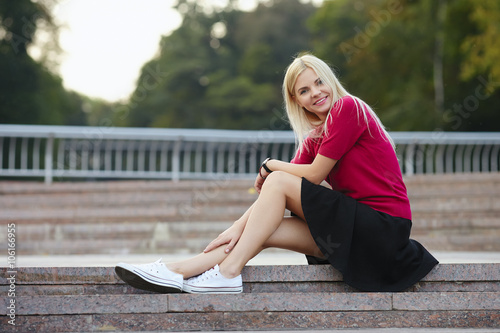 Young sporty beautiful blonde woman sitting on the park stairs and smiling © sergeyzapotylok
