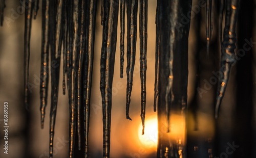 Abstract background of natural icicle formation through glass as morning sun rises.  Long icicles on a wintry January morning. Sunshine dawning through icicles that hang low from a roof s edge.