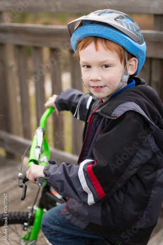 Happy little boy wearing a helmet riding a bicycle across a wooden bridge. © rachdole