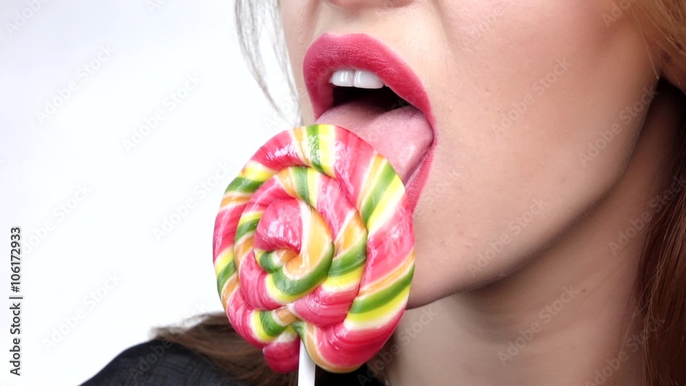 Beautiful girl's lower part of face. lips and tongue are sliding over big lollipop. Close up. Slow motion