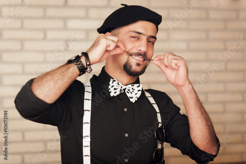 Funny face stylish hipster man twirling handlebar mustache with a playful attitude and a smile while wearing a beret, bow tie and suspenders.