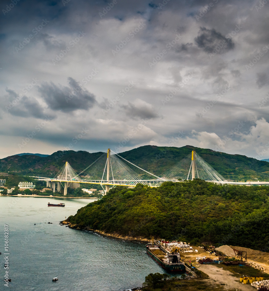 Picturesque landscape with a view on Tsing Ma Bridge, Hong Kong, China. A view with urban and industrial merging with natural mountaings on islands and gorgeous clouds.