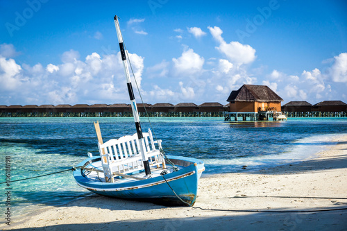 Лодка на берегу на фоне виллы на воде для новобрачных на Мальдивских островах
