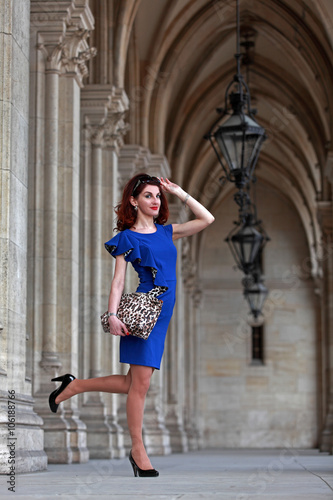 Beautiful woman with blue dress, handbag and high heels standing in gothic arcades