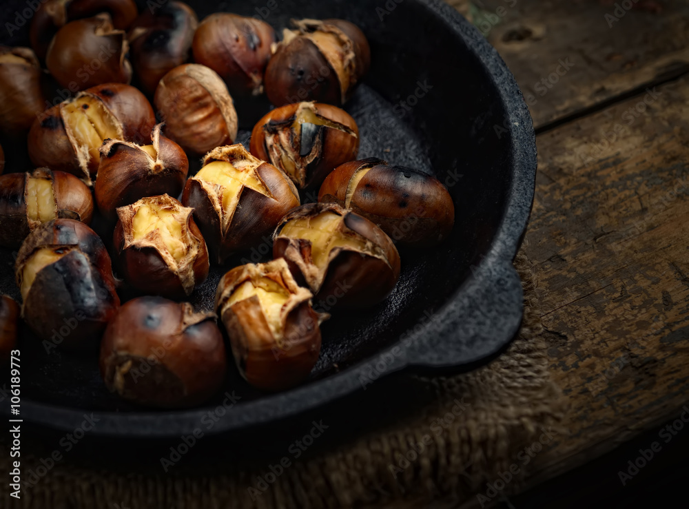 Heap of grilled edible chestnuts in cast iron skillet over dark wooden surface with textile napkin
Heap of grilled edible chestnuts in cast iron skillet over dark wooden surface with textile napkin