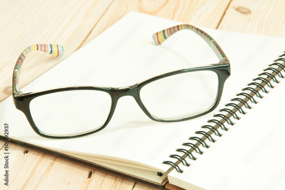 focus eyeglasses on a notebook on the wooden table , pair of gla focus eyeglasses on a notebook on the wooden table , pair of gla