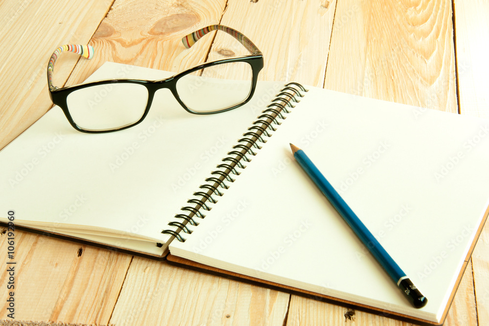 Open notebook with pencil and eye glasses on wood table backgrou Open notebook with pencil and eye glasses on wood table backgrou