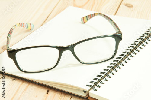 focus eyeglasses on a notebook on the wooden table , pair of gla