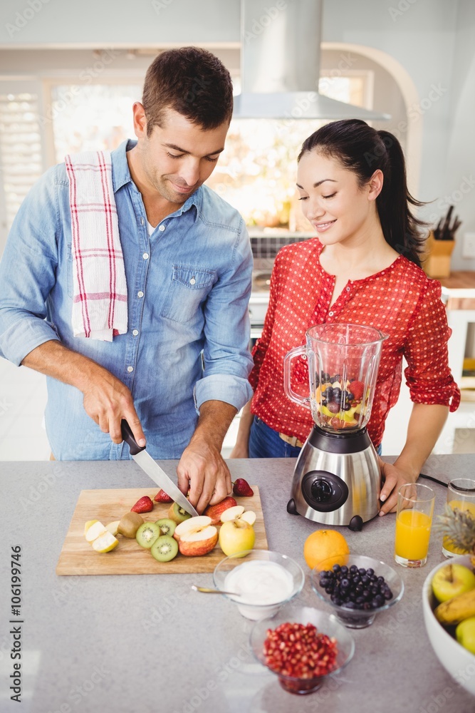 Couple preparing fruit juice while standing at table