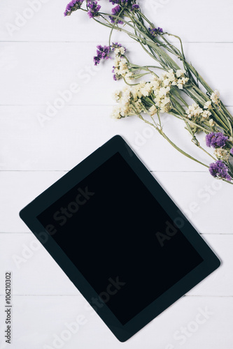 Closeup tablet with a empty blank screen monitor with a bouquet of flowers on white table background with natural wood vintage planks wooden texture top view vertical, space for publicity text