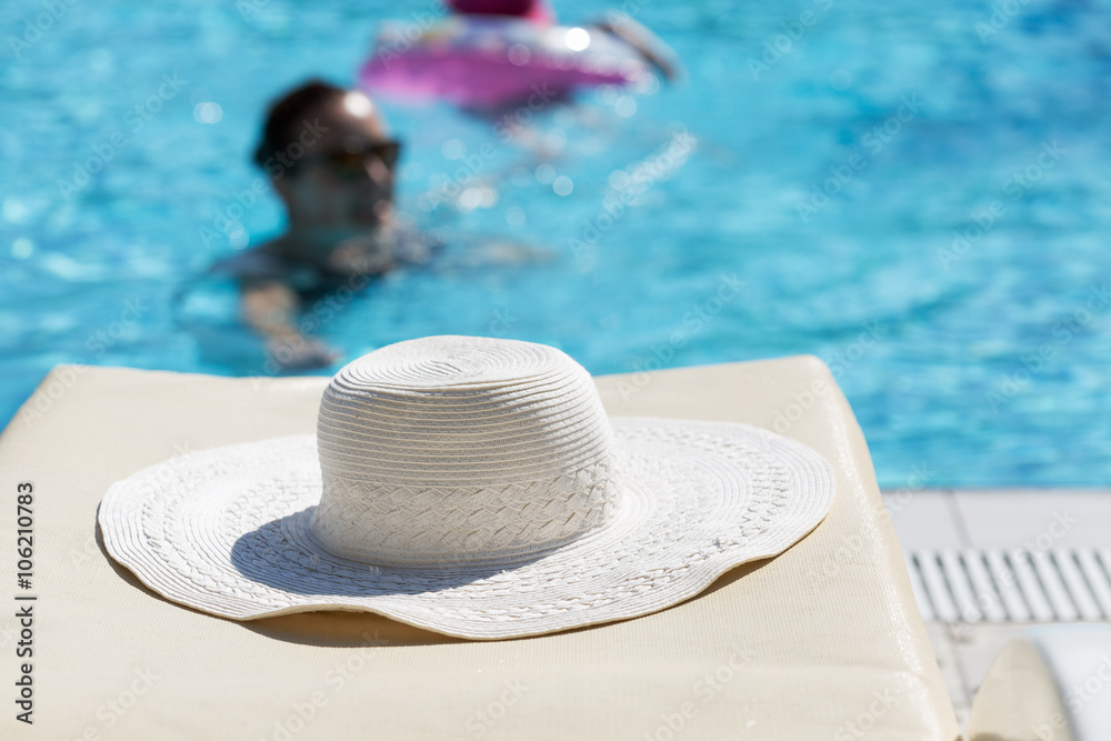 White hat left by a swimming pool with woman swimming in it. Selective focus