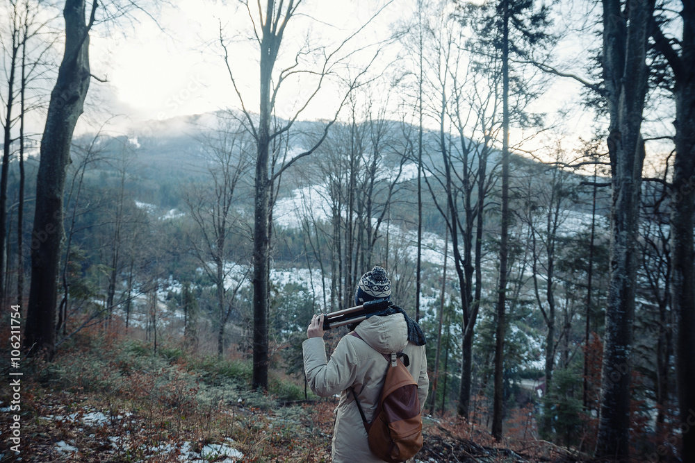 young guy in a warm cap and a jacket with a scarf on the neck, trousers and rubber boots walks alone in the Carpathian mountains with a camera, a tripod and a backpack on his shoulders young guy in a warm cap and a jacket with a scarf on the neck, trousers and rubber boots walks alone in the Carpathian mountains with a camera, a tripod and a backpack on his shoulders