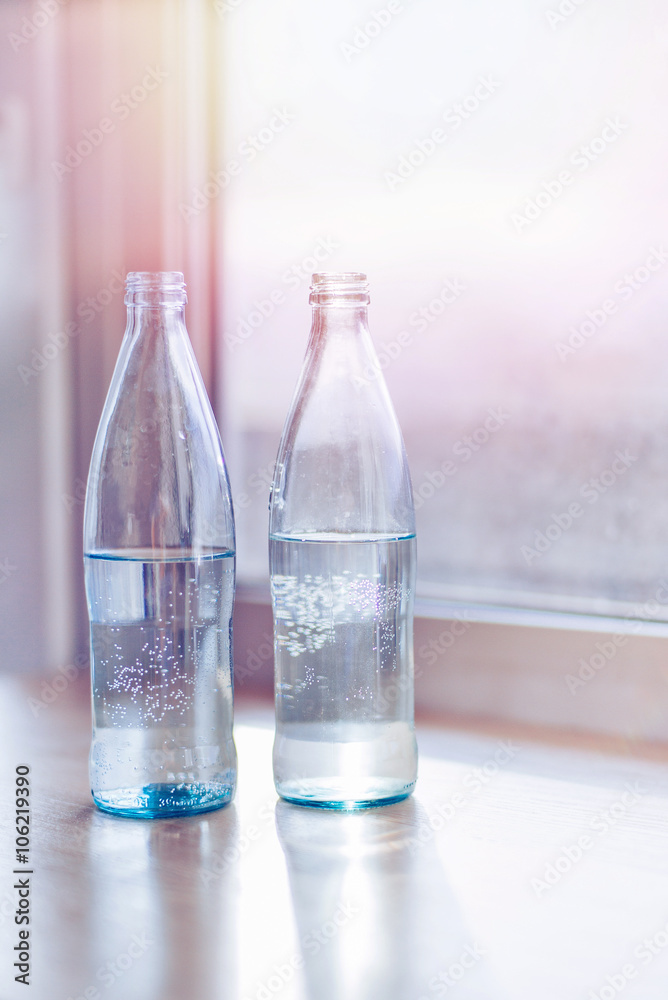 Glass bottles with pure water with sunlight. Film effect.