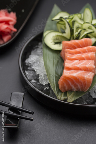 Salmon sashimi on a bamboo list and ice over black background
