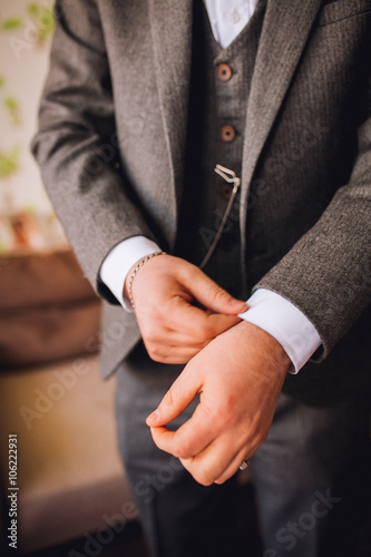 Stylish and handsome groom in waistcoat tying his bow-tie in the morning of the wedding day. Groom with beard