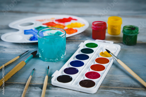 Set of watercolor paints, brushes for painting and palette on old vintage wooden background