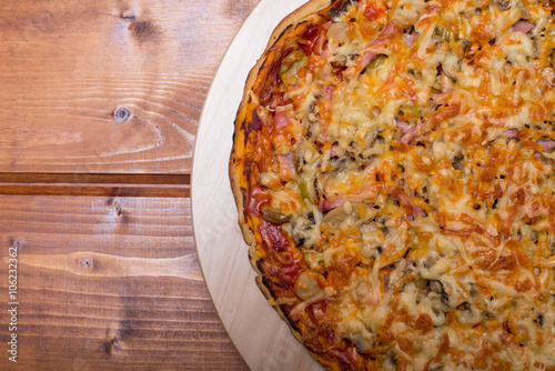 Flat lay Italian pizza with ham and mushrooms on a wooden round tray on wooden table top view