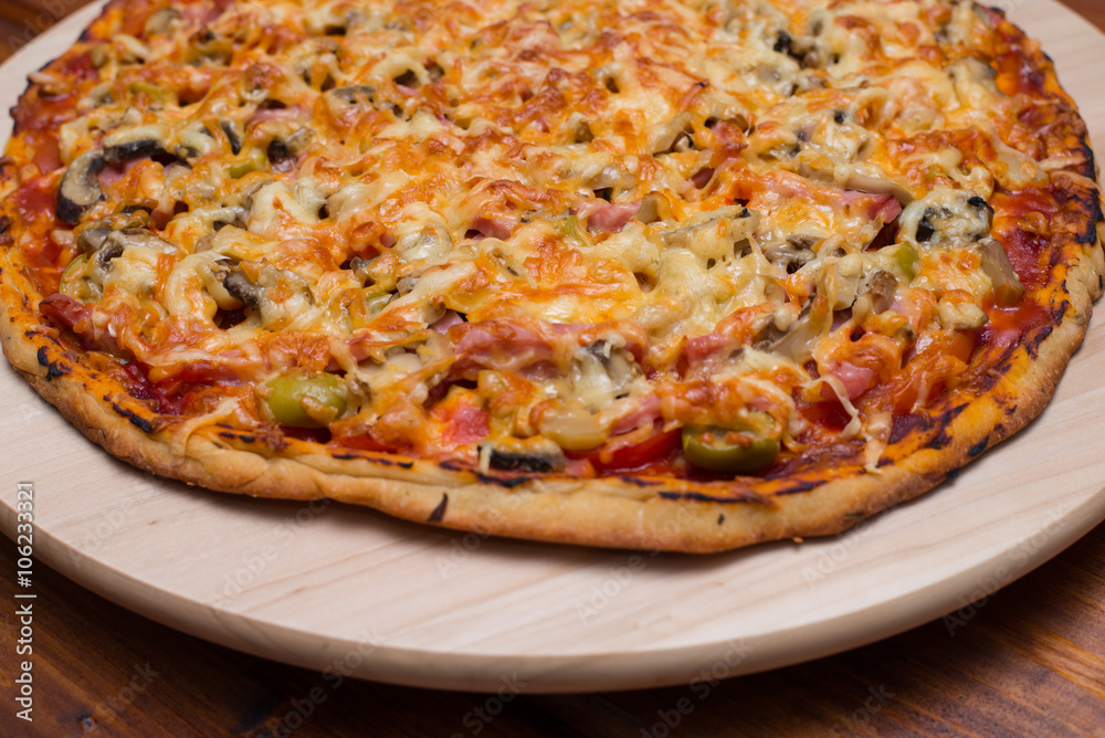 Italian pizza with ham and mushrooms on a wooden board on natural wooden table Italian pizza with ham and mushrooms on a wooden board on natural wooden table
