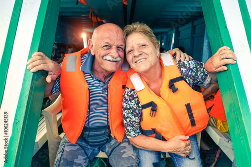 Senior couple with life jacket traveling on tropical boat excursion - Active elderly tourists having fun ready to sail - Happy retired friends on island tour - Concept of travel and joyful retirement 