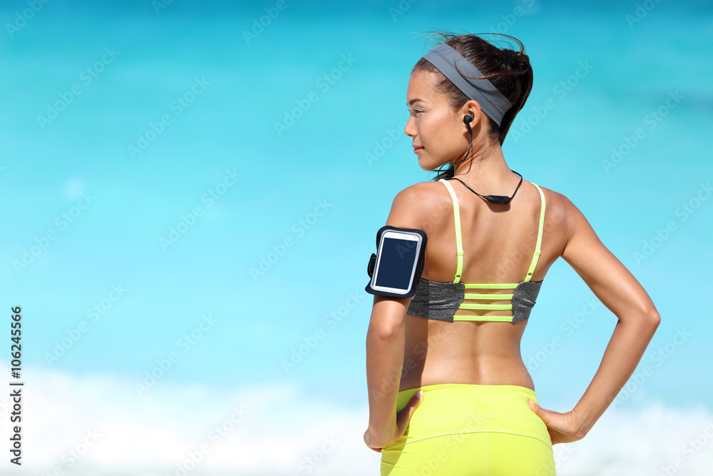 Fitness runner woman with fit back wearing phone armband wireless headphones on ocean background. Multiracial exercise girl jogging on summer beach with sports smartphone touchscreen for app. Stock Photo | Adobe