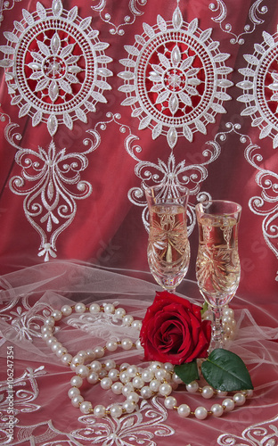 two glasses of champagne and red rose on red satin and white tul