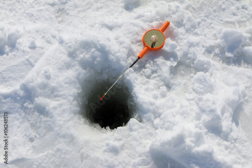 Fishing by a winter plastic rod in the ice hole on the pond