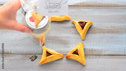 Woman hand placing a Purim basket (Mishloach manot) in side a Star of David made out of Purim Cookies - Hamentashen (Ozen Haman) for Purim Jewish Holiday. Copy space photo