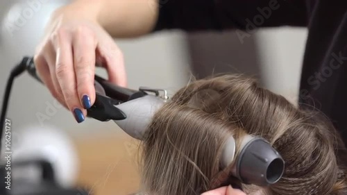 Stylist curling hair for young woman. Slow motion. Close up