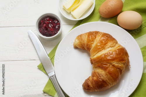 Sunday breakfast with croissant, jam and egg, green napkin on white painted wooden table, copy space