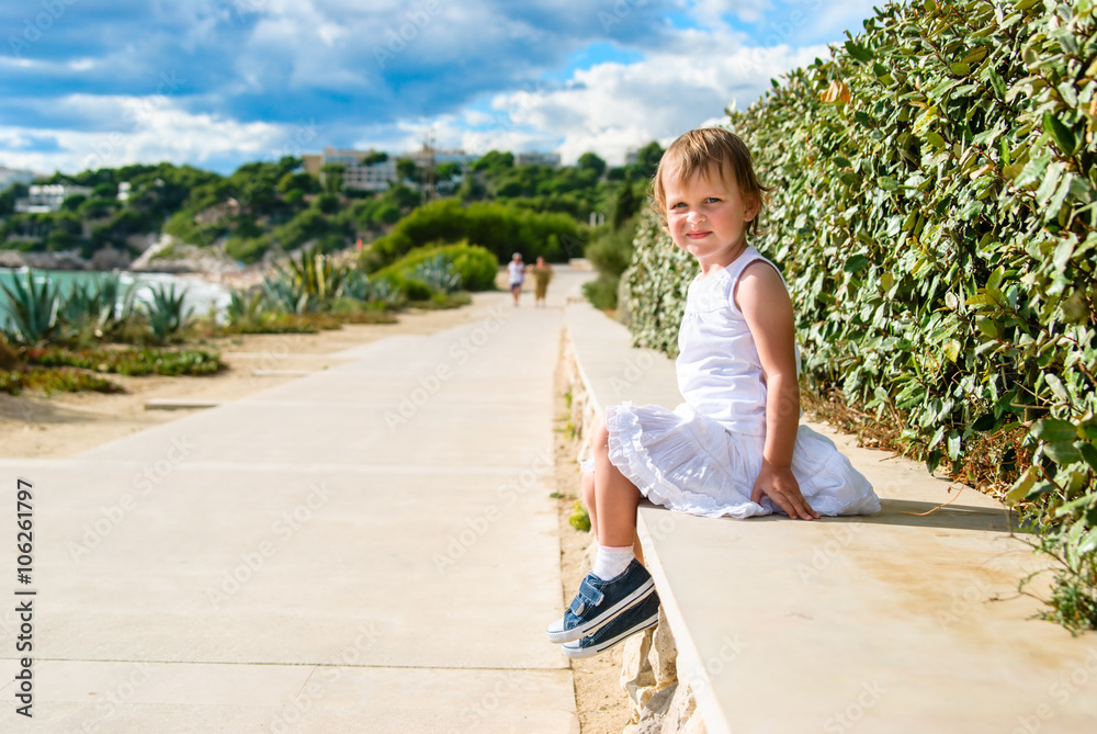 Girl sits on a stone wide curb on the beach