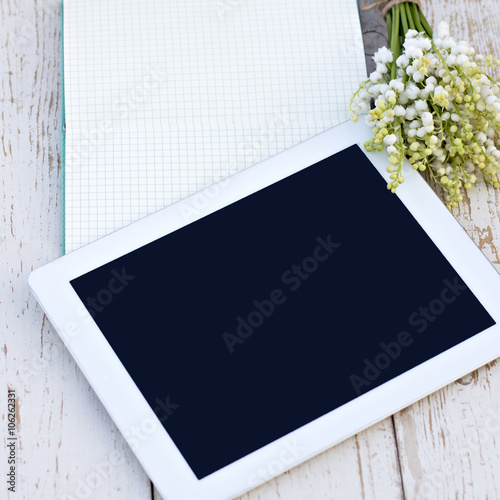 diary, a tablet computerand  lilies of valley on the table photo