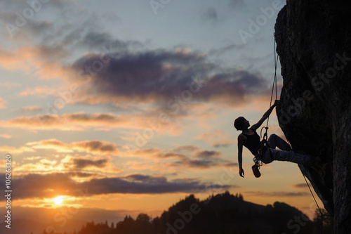 Foto Silhouette of beautiful athletic woman climbing steep rock wall against amazing sunset scene in the mountains