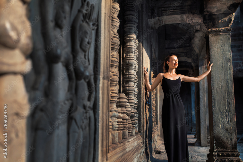 Fototapeta premium Cambodia Tourist Attraction. Happy Beautiful Religious Young Woman Relaxing In Corridor At Prasat Angkor Khmer Wat Temple, Siem Reap. Famous Landmark, Travel Destination. Harmony, Tranquility Concept
