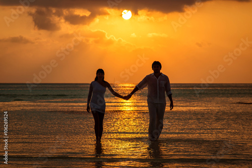 Счастливая влюбленная пара идет по воде на закате держась за руки