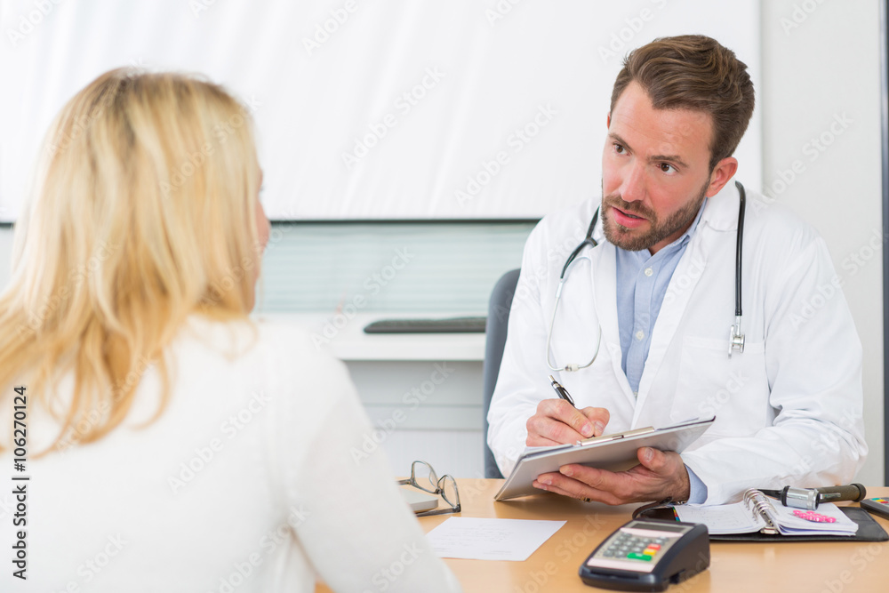 Young attractive doctor taking notes while patient speak Young attractive doctor taking notes while patient speak