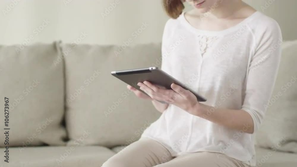 Beautiful young woman is using a tablet computer while sitting on a couch at home. Shot on RED Cinema Camera. Beautiful young woman is using a tablet computer while sitting on a couch at home. Shot on RED Cinema Camera.
