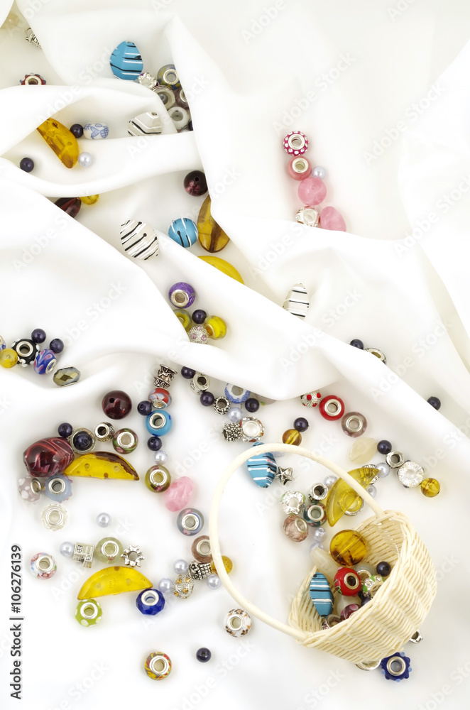 Basket of beads dropped on soft white textile background Basket of beads dropped on soft white textile background