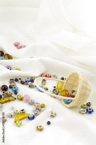 Basket of beads dropped on soft white textile background