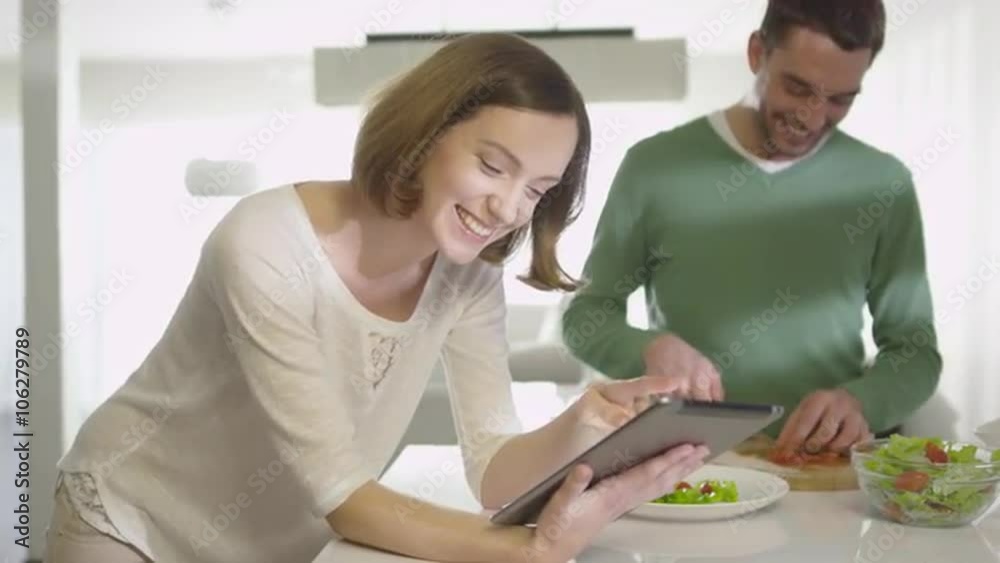 Happy couple is preparing healthy food in the kitchen at home while checking a tablet computer. Shot on RED Cinema Camera. Happy couple is preparing healthy food in the kitchen at home while checking a tablet computer. Shot on RED Cinema Camera.