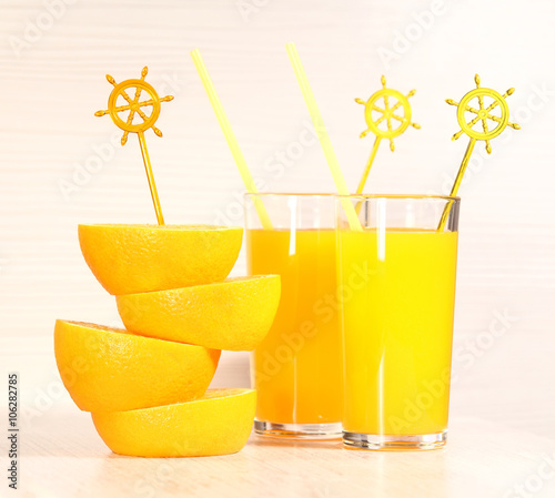 Fresh orange lemonade or juice in a glass next to the whole fruit and orange slices on a light gray background