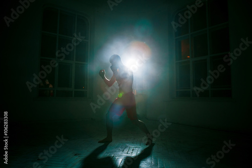 The young man kickboxing on black background