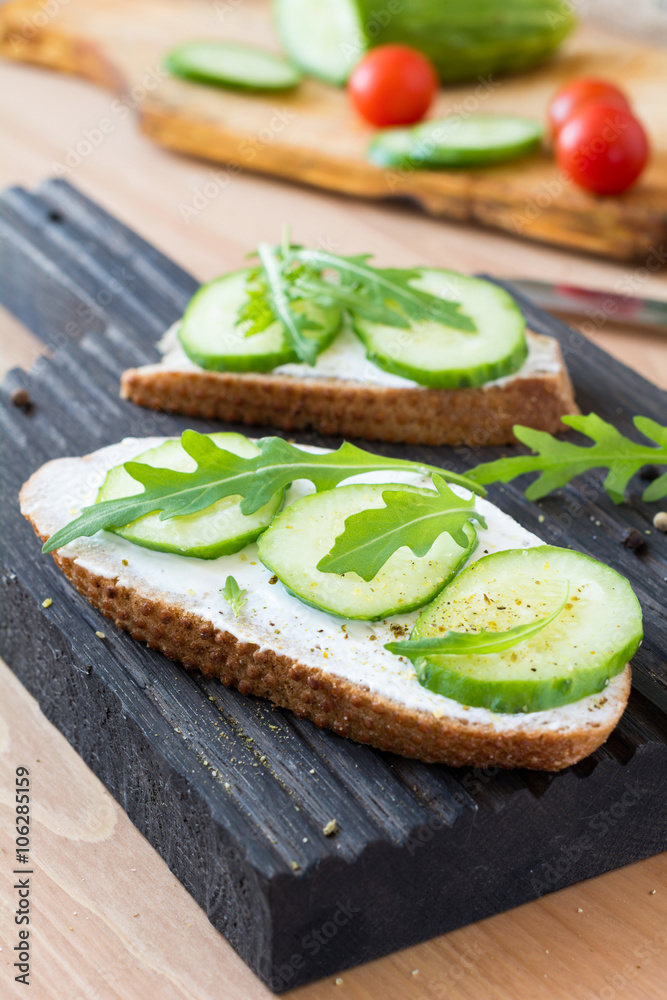 Healthy breakfast or snack: Cucumber, cream cheese and arugula toast on wooden cutting board