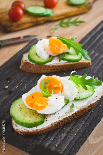 Cucumber and egg toast with arugula and cream cheese. Tasty breakfast or snack on wooden cutting board. Selective focus